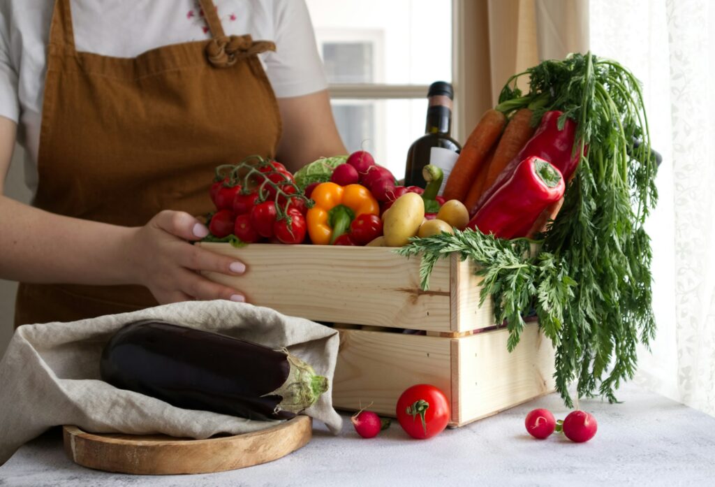 A box with food products on the table and female hands prepare vegetables for delivery